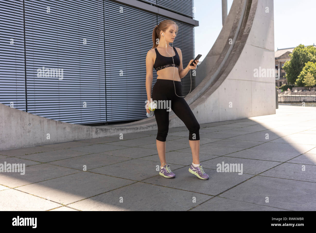Young woman taking break from exercise and using smartphone in city, Berlin, Germany Stock Photo