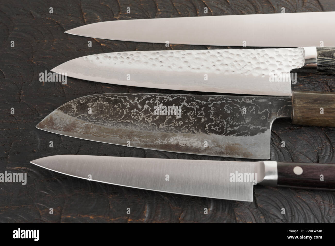 Four new and used knives on black cutting board Stock Photo