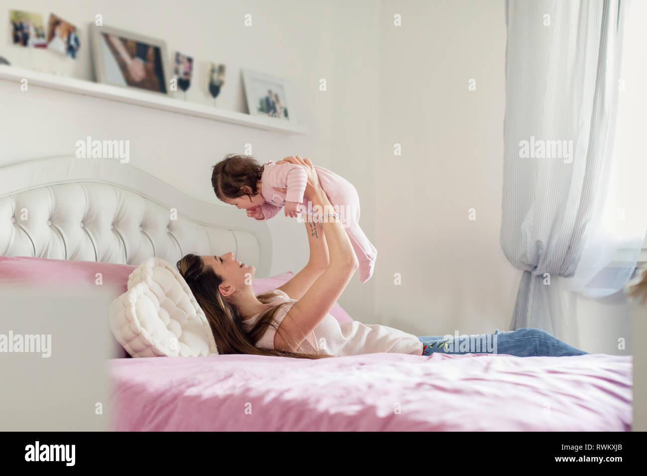 Mother playing with baby girl in bed Stock Photo