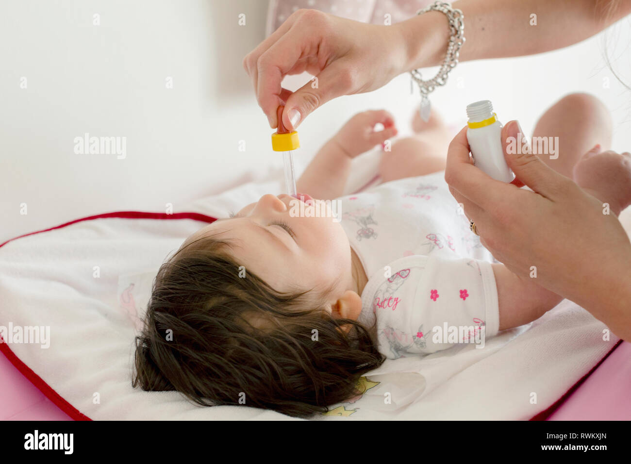 Mother feeding baby girl medicine in bed Stock Photo