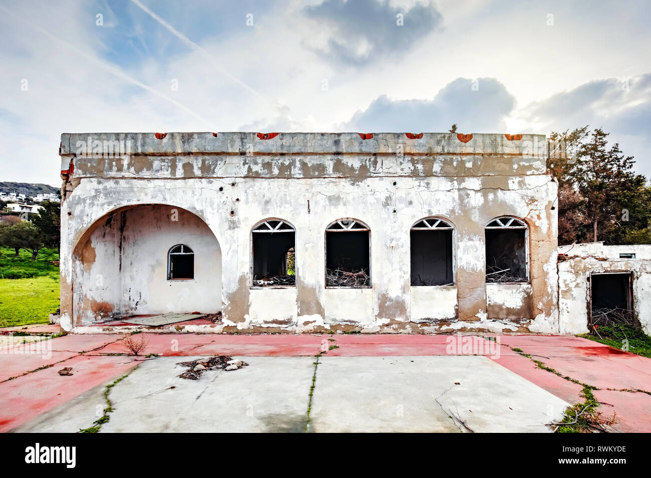 Exterior of an abandoned old white concrete single story house in a rural meadow field. Stock Photo