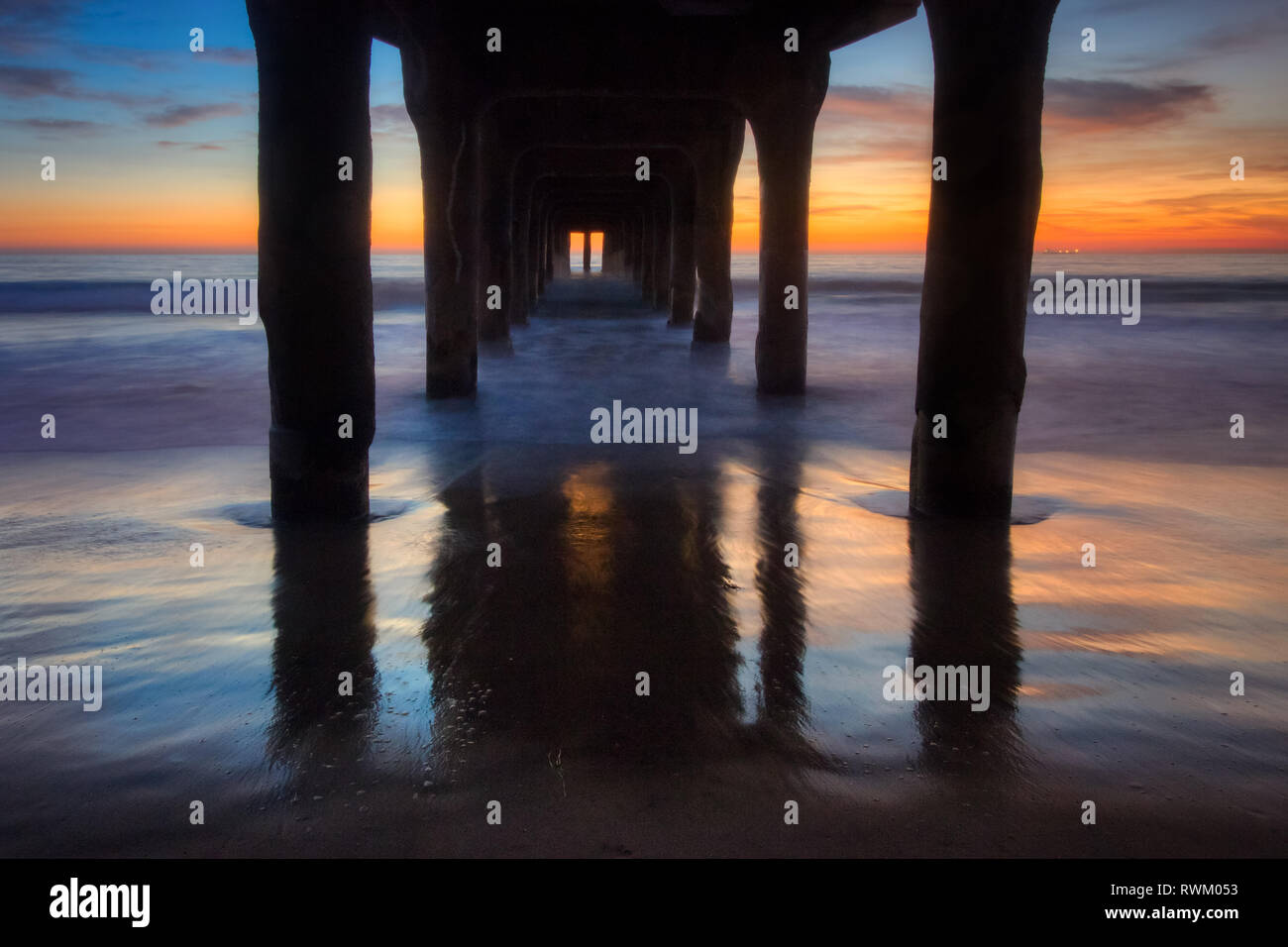 Long-exposure shot from under Manhattan Beach Pier after sunset with colorful sky and smooth waves washing onto the beach, Manhattan Beach, California Stock Photo
