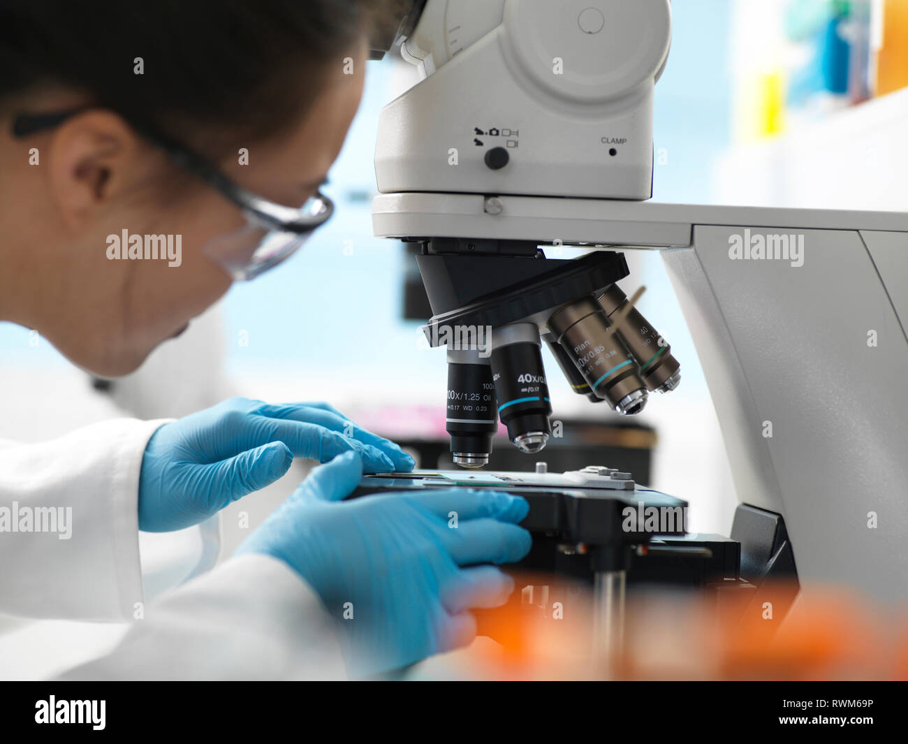 Scientist placing human sample on glass slide under microscope in laboratory Stock Photo