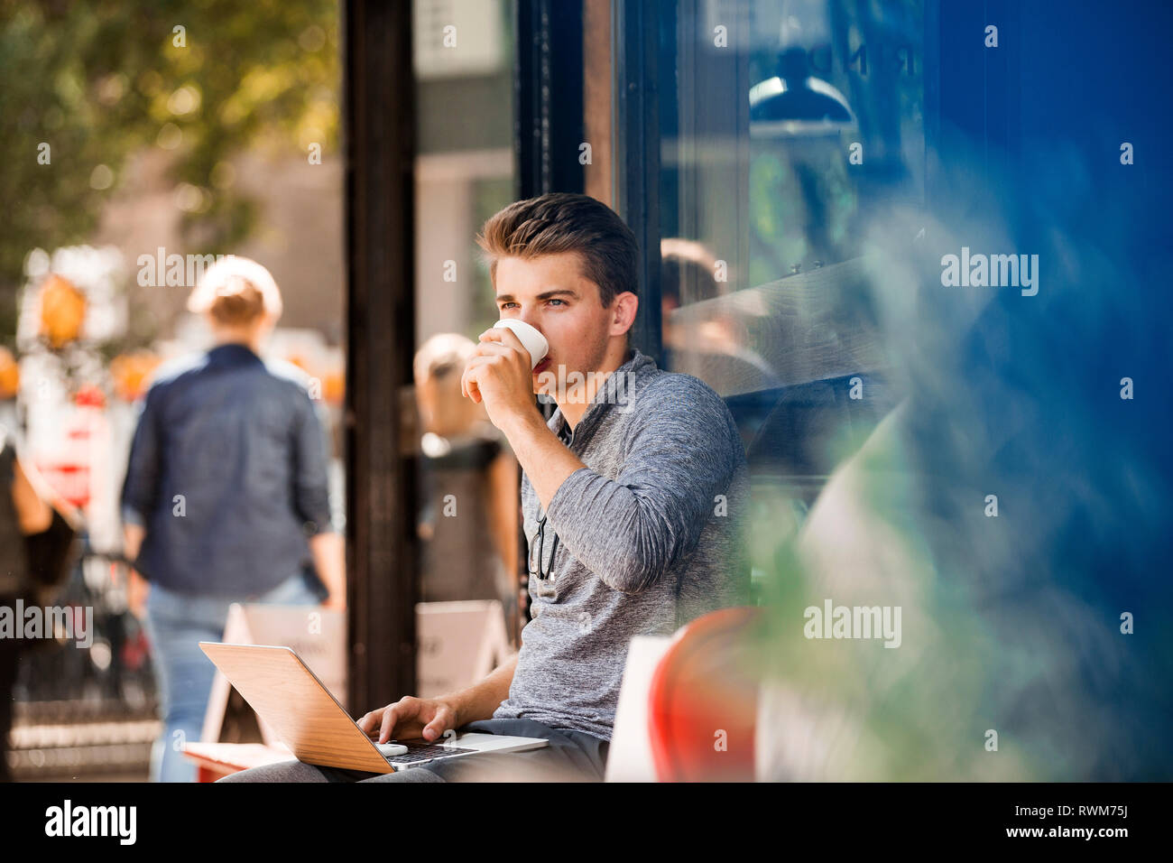 Young man drinking coffee and using laptop at cafe Stock Photo