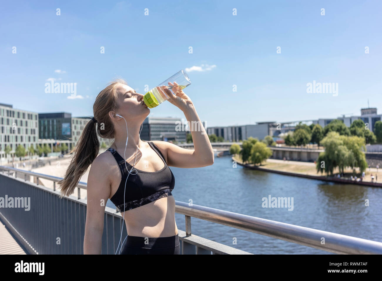 Young woman taking break from exercise and drinking water in city, Berlin, Germany Stock Photo