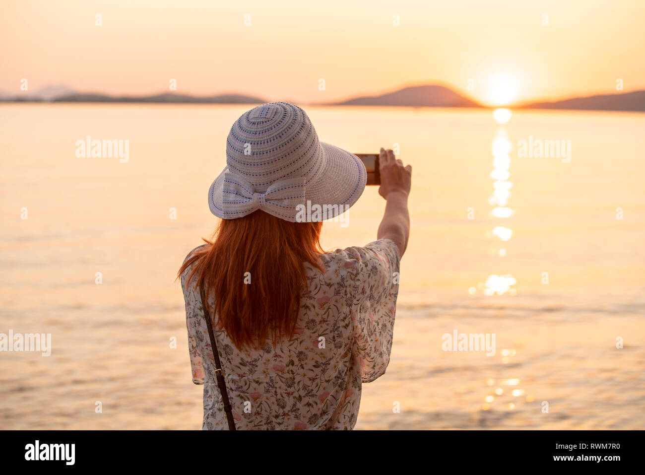 Tourist taking photograph of sunset on beach Stock Photo