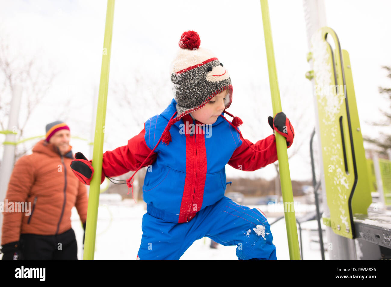 Boy with father climbing up playground slide in snow Stock Photo