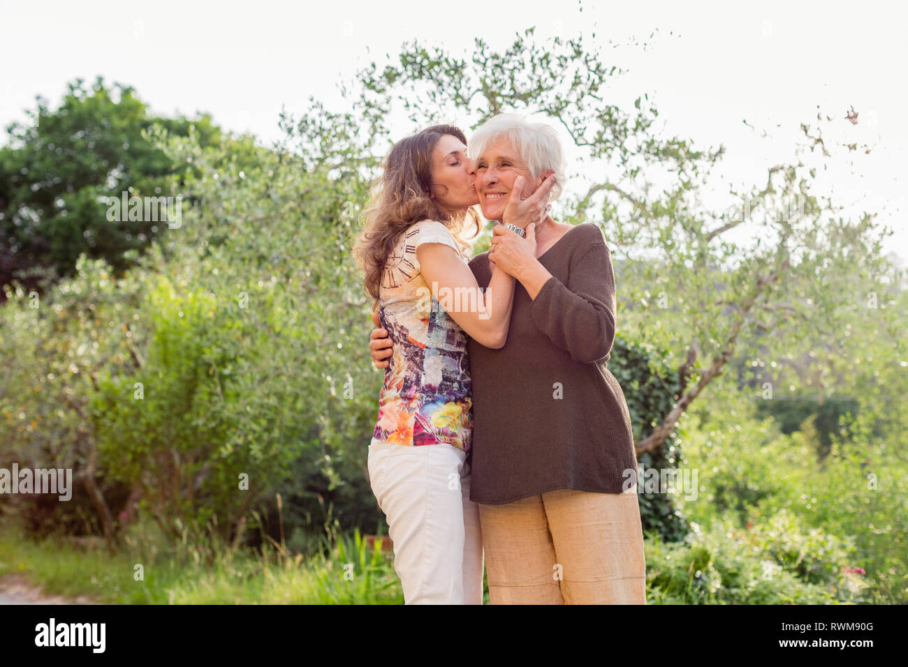 Mature woman kissing mother on cheek in garden Stock Photo