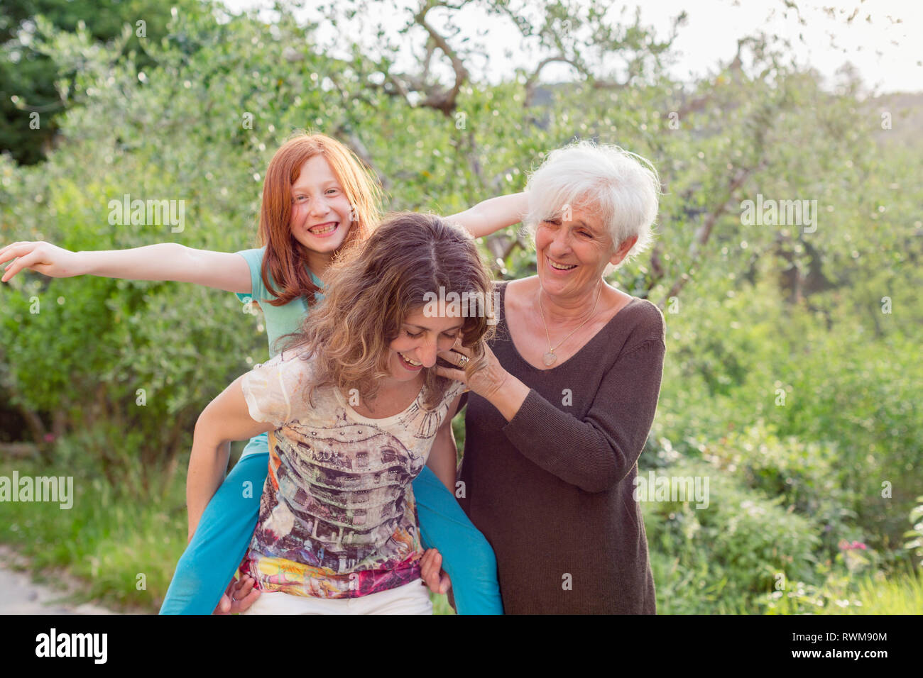Girl getting piggyback with mother and grandmother in garden Stock Photo