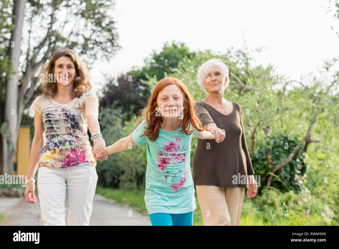 Girl on rural road holding hands with mother and grandmother, portrait Stock Photo