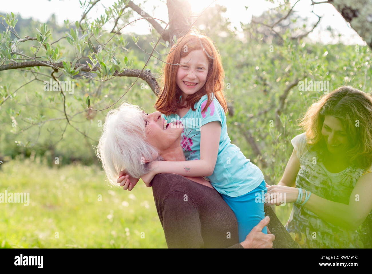 Girl getting carried by grandmother, with mother in garden Stock Photo