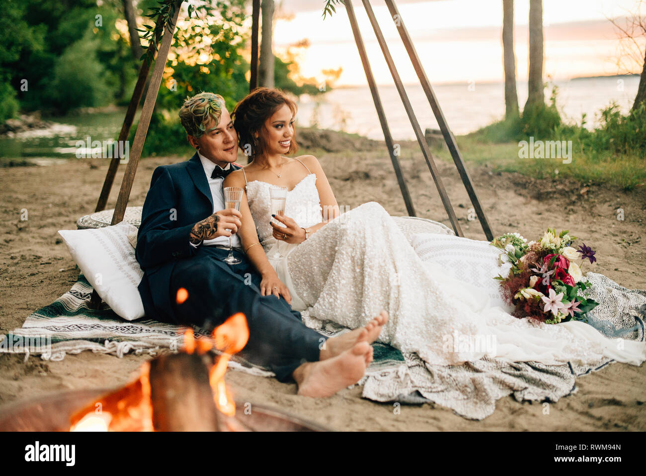 Bride and groom on picnic blanket by lakeside campfire, Lake Ontario, Toronto, Canada Stock Photo