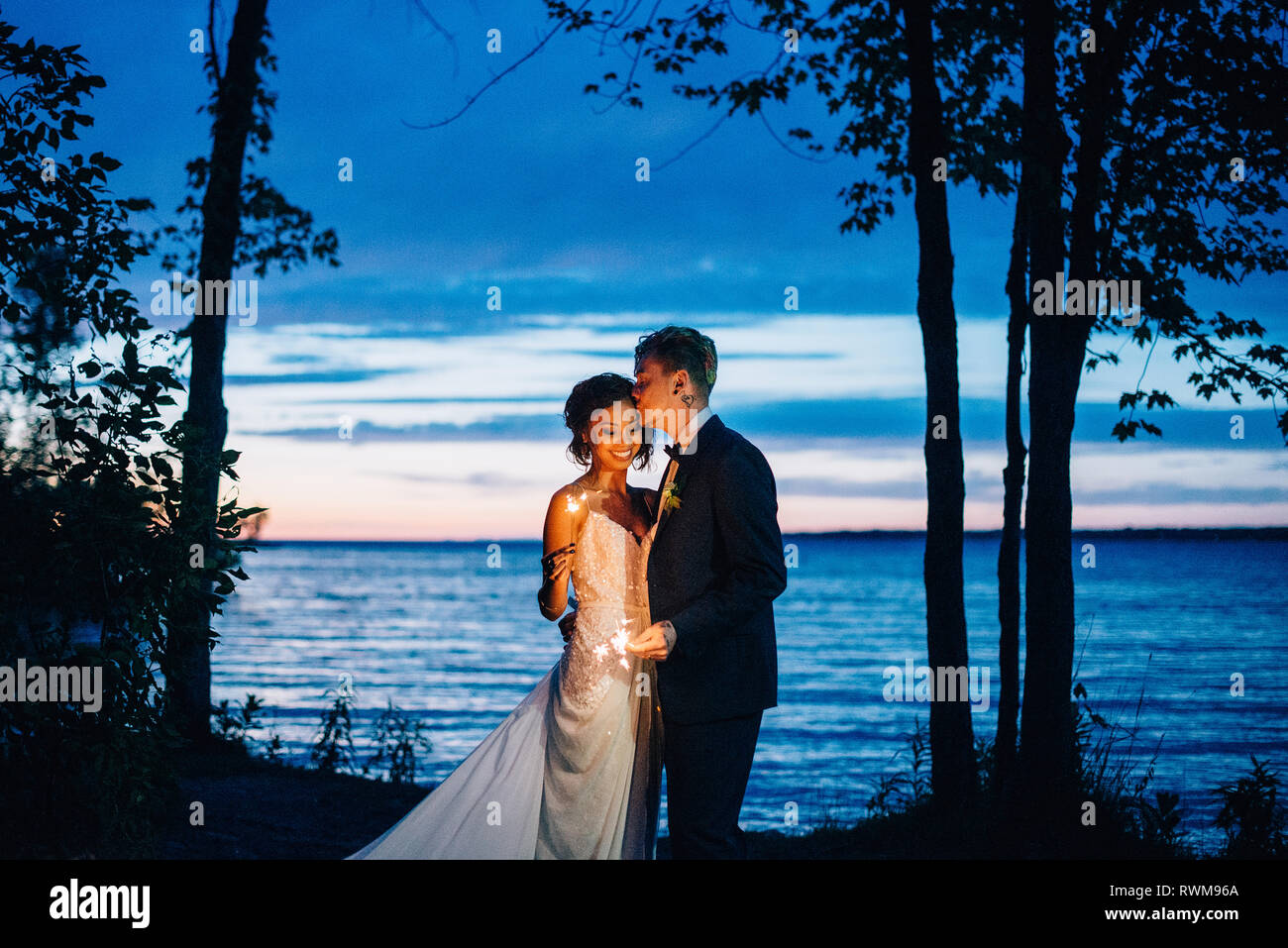 Romantic bride and groom with sparklers by lakeside at dusk, Lake Ontario, Toronto, Canada Stock Photo