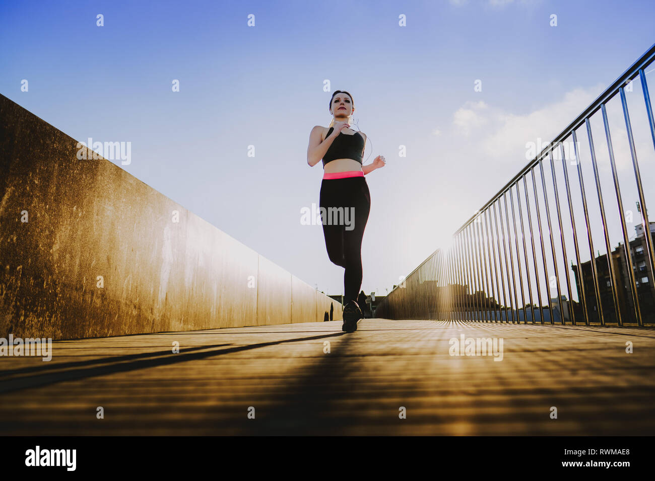 Young lady in sportswear running on footpath of a bridge in sunny weather  with blue heaven Stock Photo - Alamy