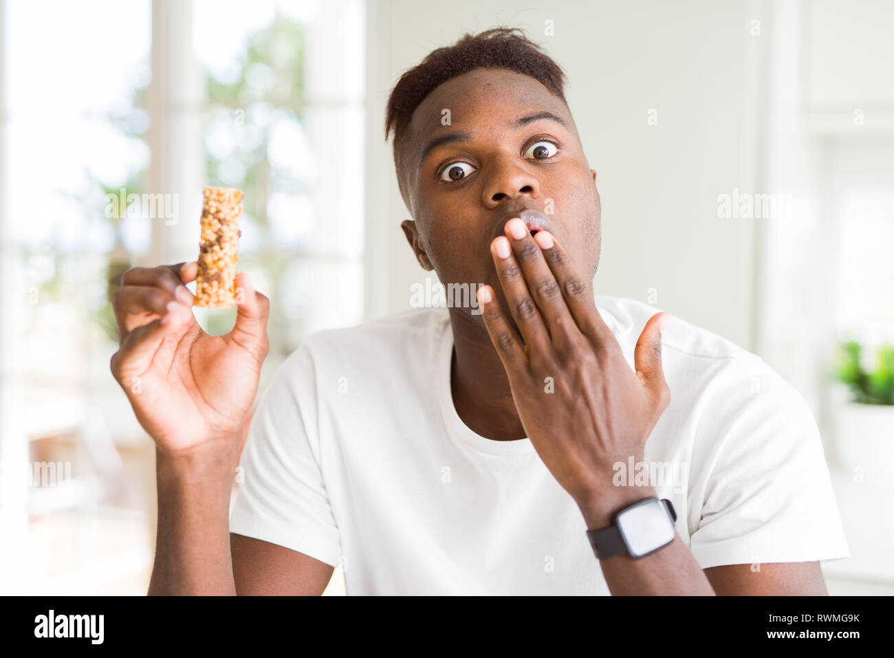 African american man eating energetic cereals bar cover mouth with hand