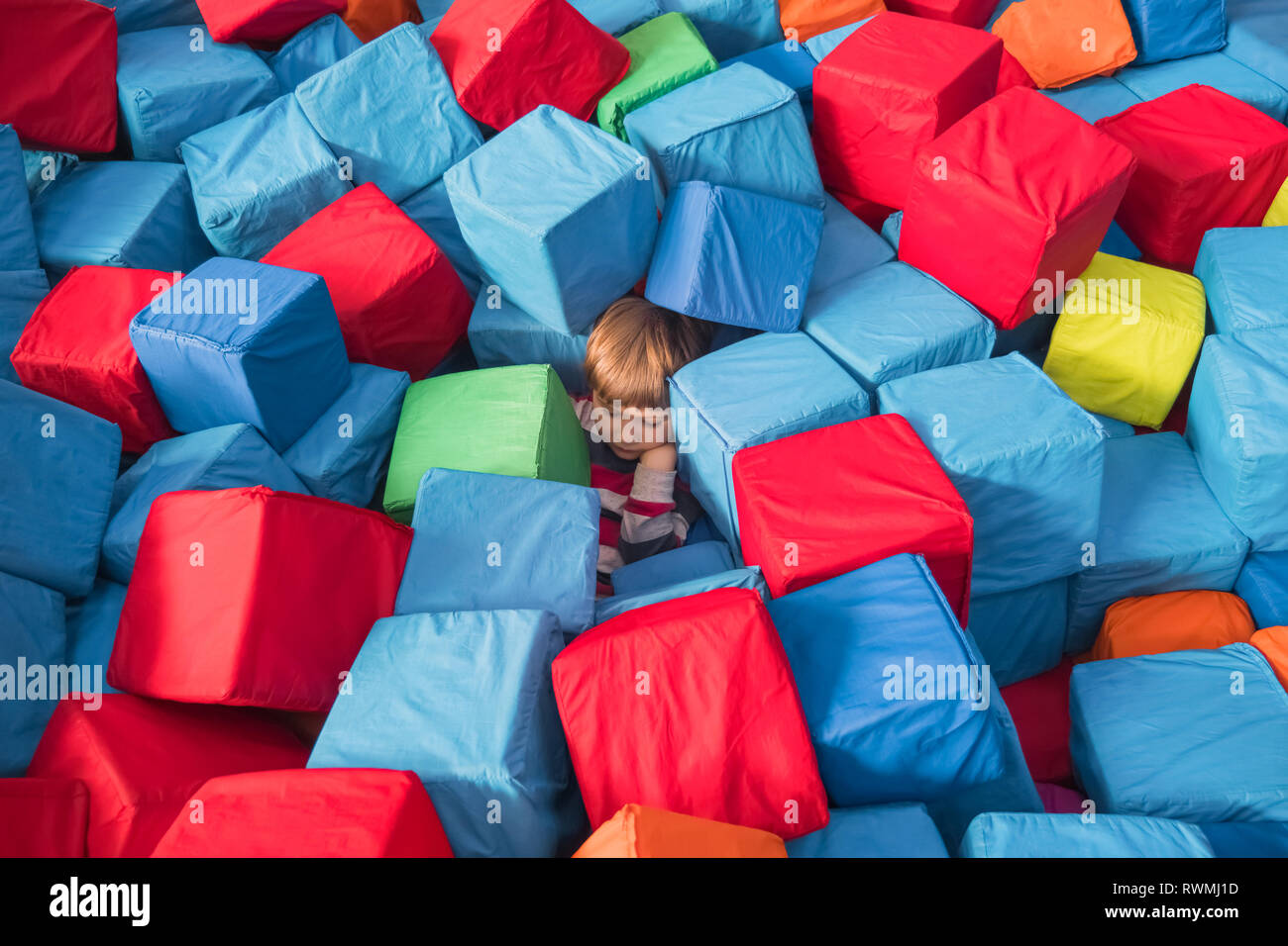 Child autism Child psychology conceptual. Boy covered up with colorful soft blocks, cubes. Children's physiological and psychological health Stock Photo