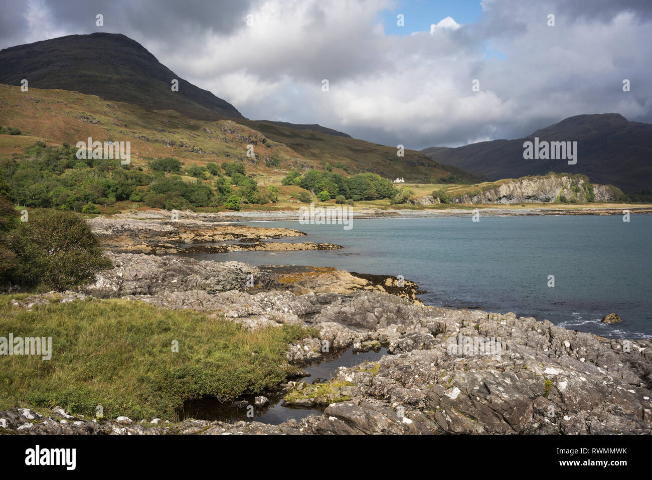 Looking towards Loch Buie Village along a rocky shore on the Island of Mull with  Ben Buie in partial sunlight. Stock Photo