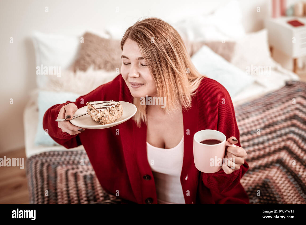 Long-haired woman in red cardigan being happy with sweet cake Stock Photo