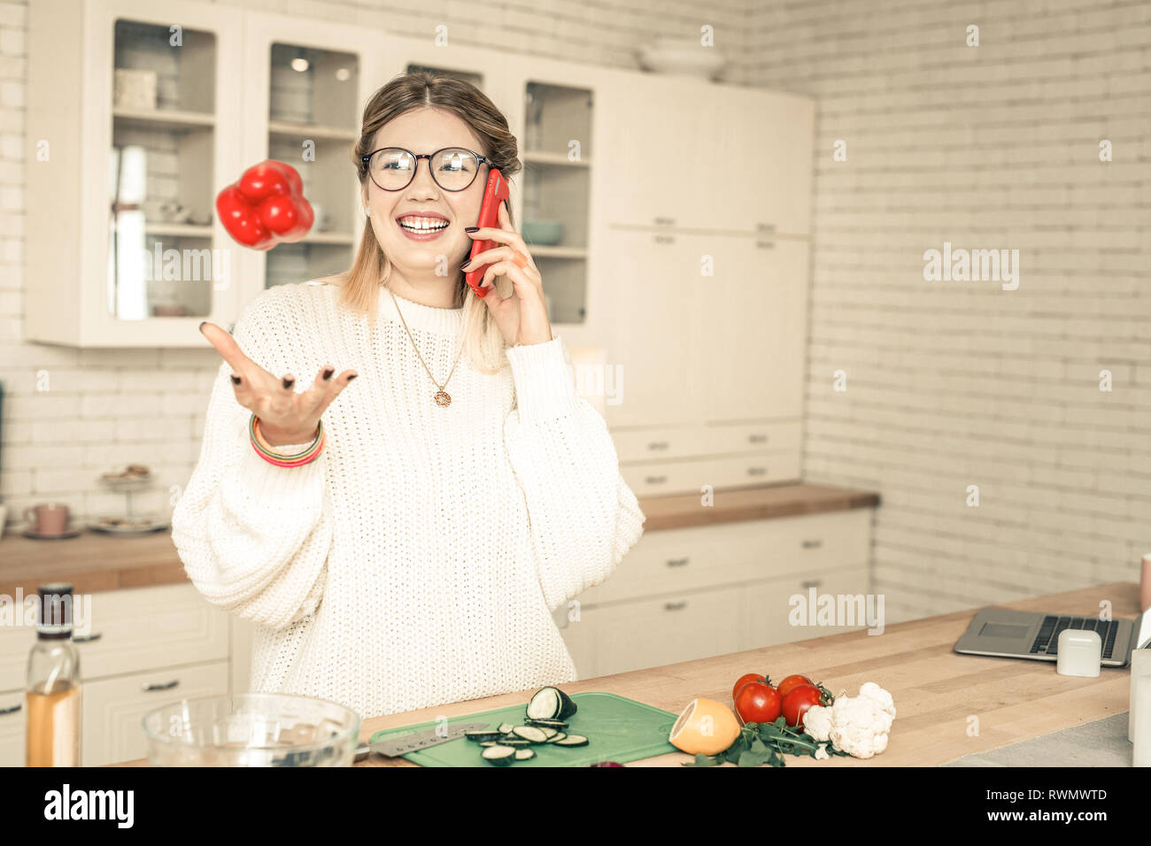Chatty lady playing with vegetables while talking on mobile phone Stock Photo