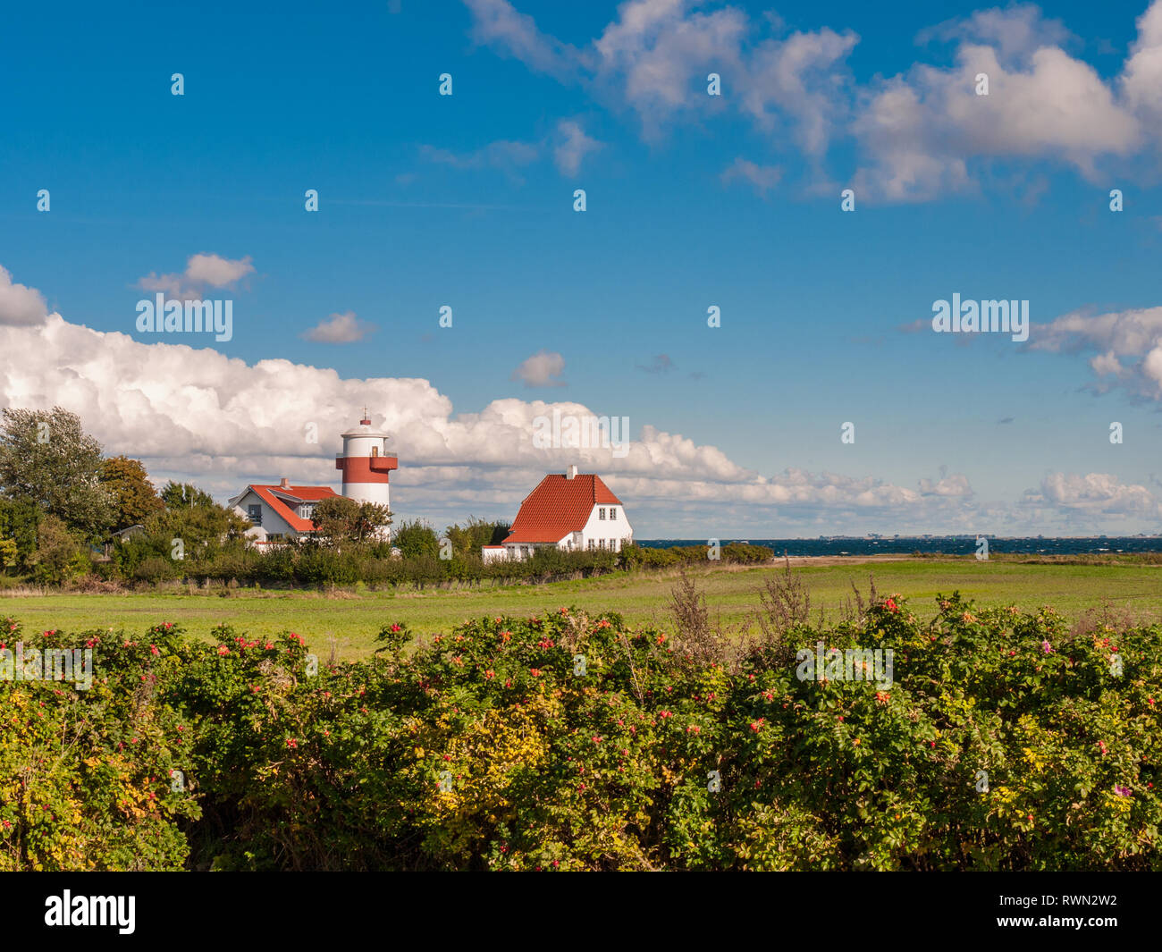 Small red and white colored lighthouse with a field in front of a wild blue sky near Lohals on Langeland island, Denmark Stock Photo