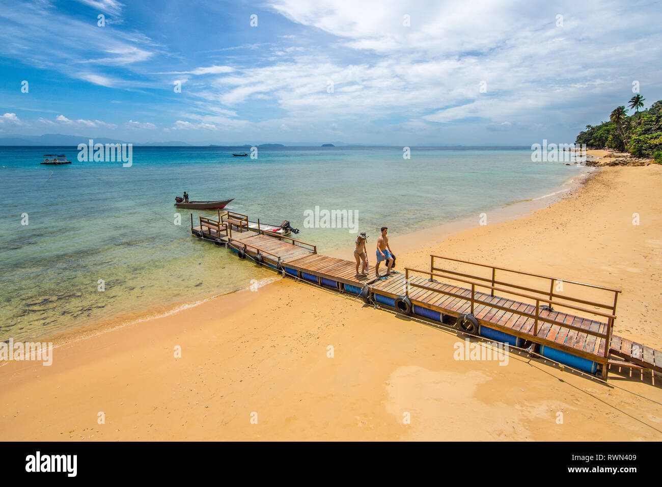 A couple arrive on a golden sand beach of a paradise island along a jetty. Stock Photo