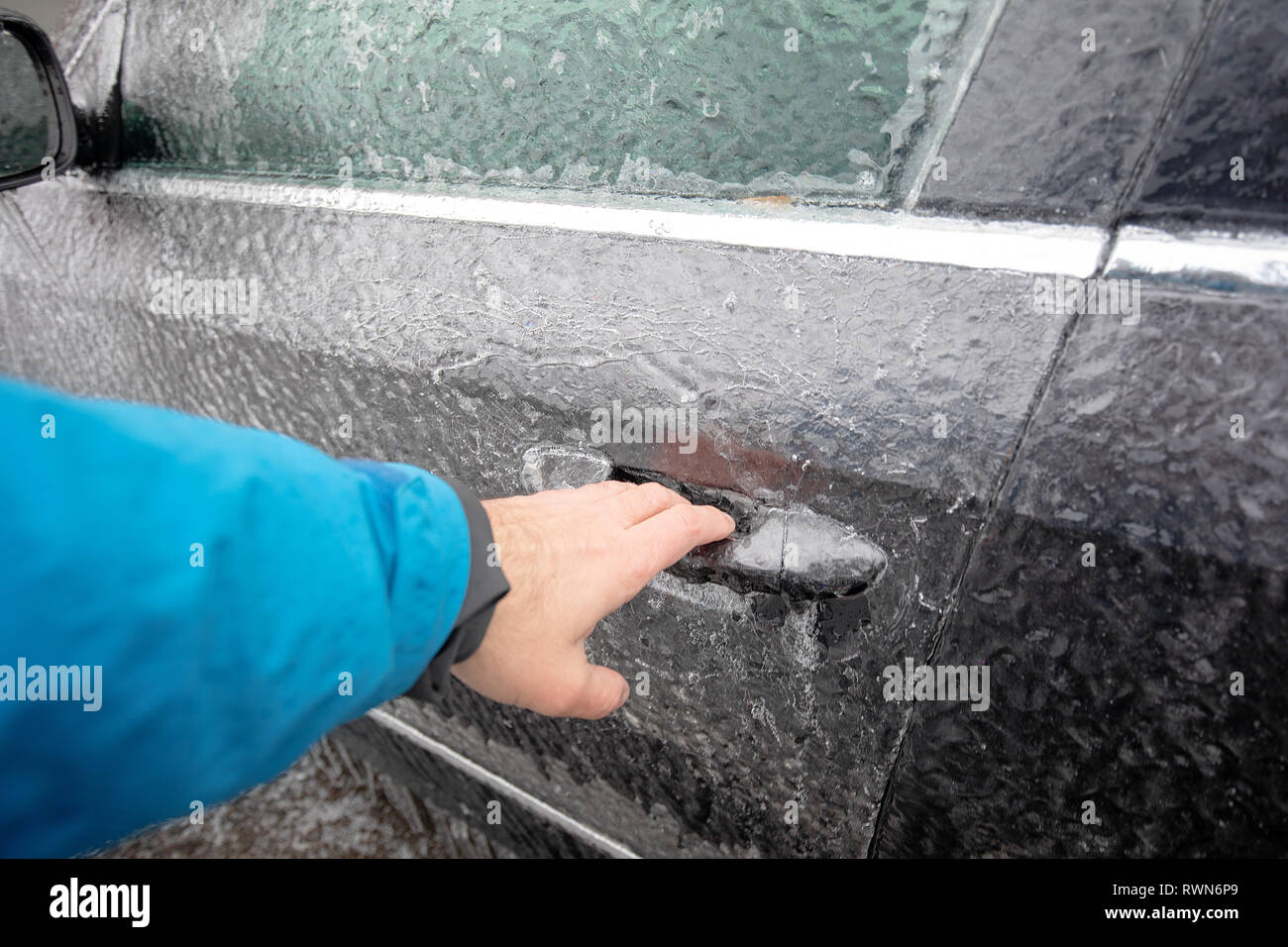 Transportation, winter, weather, vehicle concept. Hand on Car's door handle covered in snow and icy rain in winter. Blizzard Snowfall icy rain for wea Stock Photo