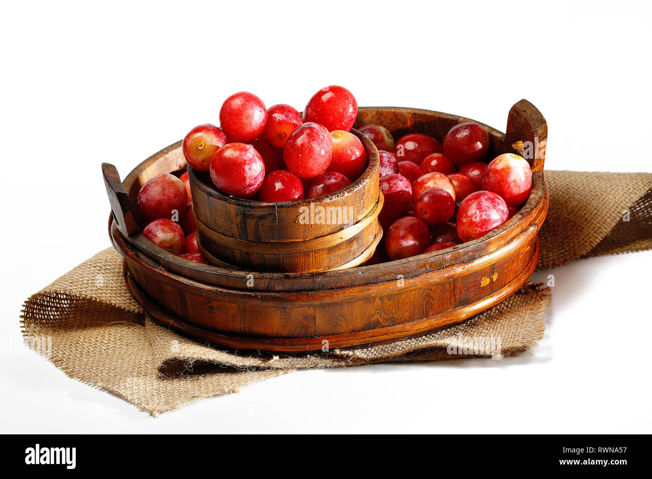 Red Mirabelle plum in basket on white background. Known as mirabelle prune or cherry plum, is a cultivar group of plum trees of the genus Prunus. Stock Photo