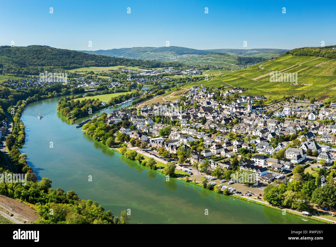 View of riverside village with bend in the river and steep vineyard slopes in the background and blue sky; Bernkastel, Germany Stock Photo