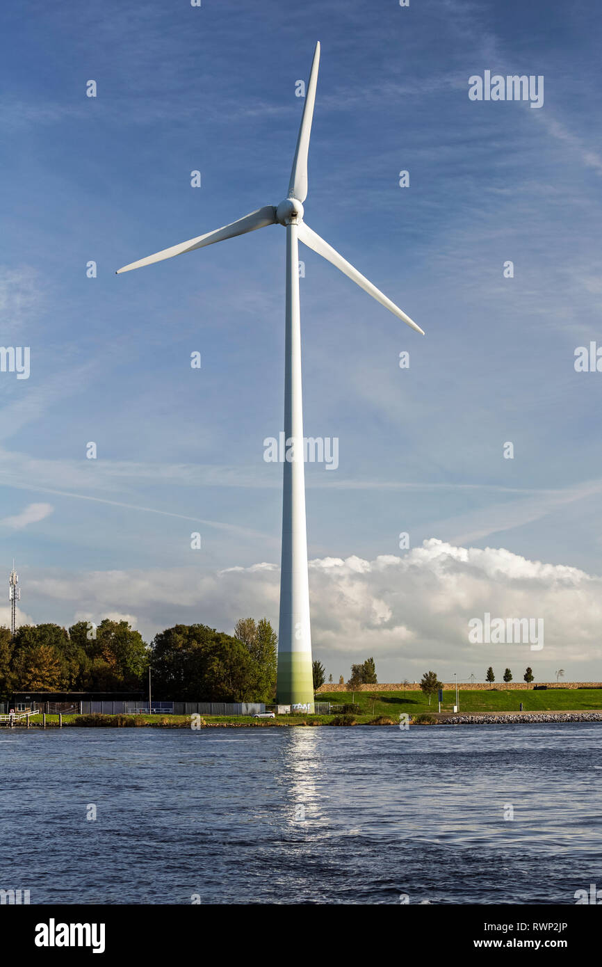 Large metal wind turbine on riverbank with blue sky and clouds; Spaarndam, Netherlands Stock Photo