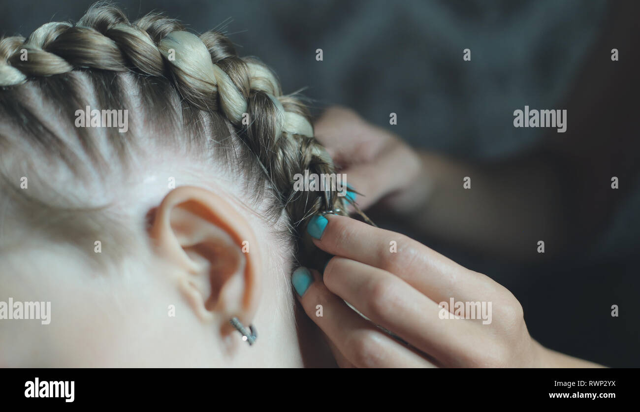 the process of braiding boxer braids on the girl's head, the master makes her hair in a beauty salon, hands close-up Stock Photo
