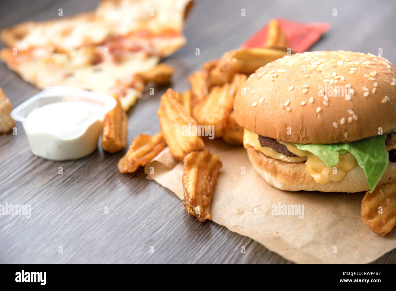 Fast food. Hamburger, french fries deluxe, pizza, cheese, lettuce and sour cream sauce. Stock Photo