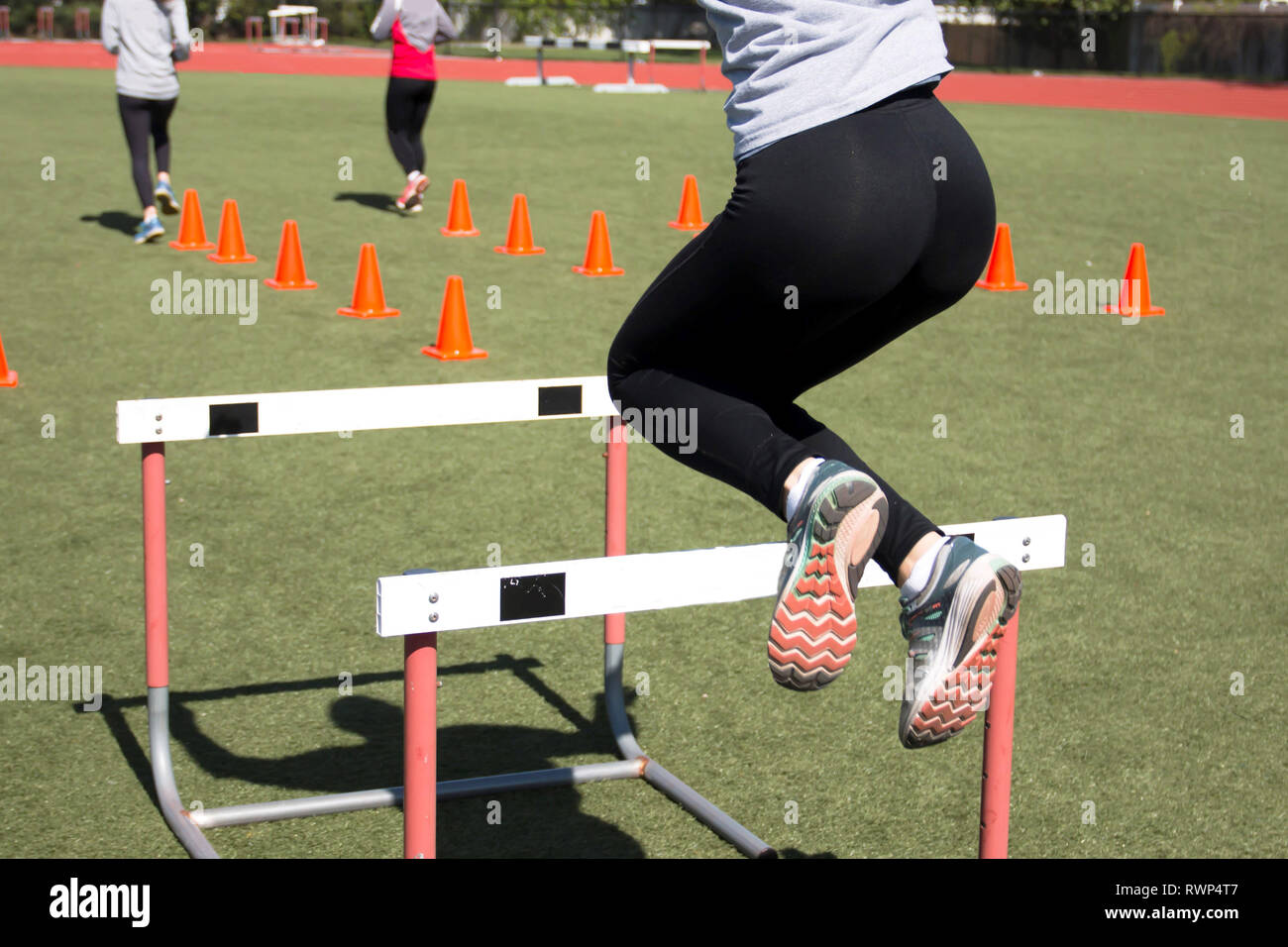 A female athlete jumping over track hurdles during track and field practice Stock Photo