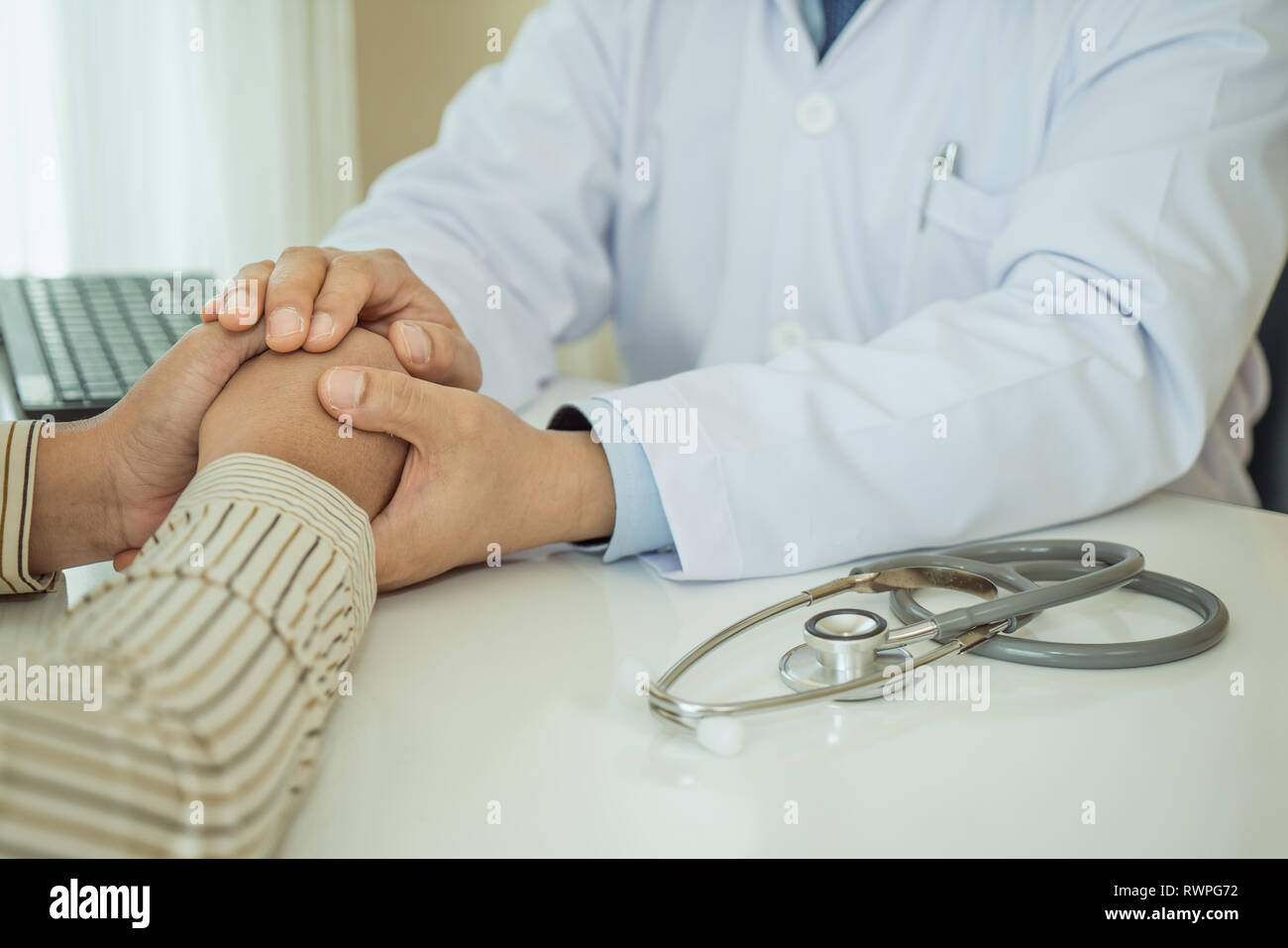 Friendly man doctor hands holding patient hand sitting at the desk for encouragement, empathy, cheering and support while medical examination. Bad new Stock Photo