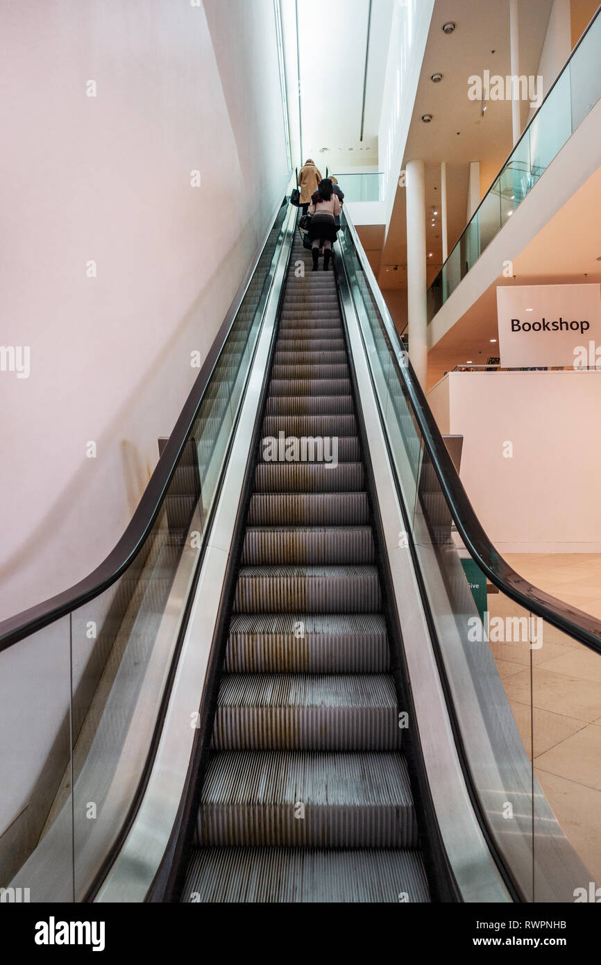 looking up at two people at the top of a steep Escalator, in the Portrait Gallery, London Stock Photo