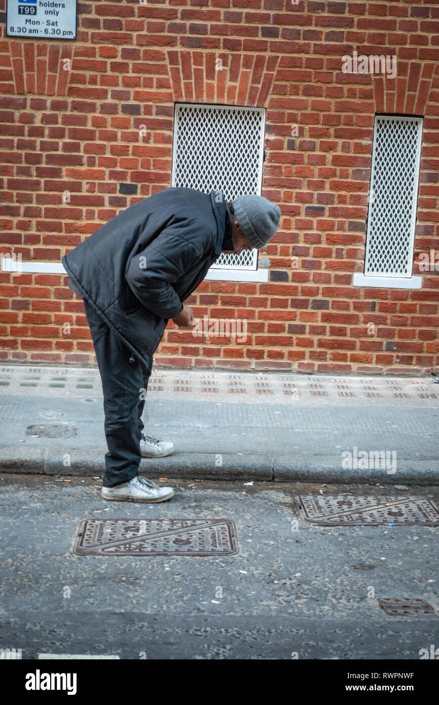 homeless people london street Older man bending down searching the street gutter for used and discarded cigarette ends Stock Photo
