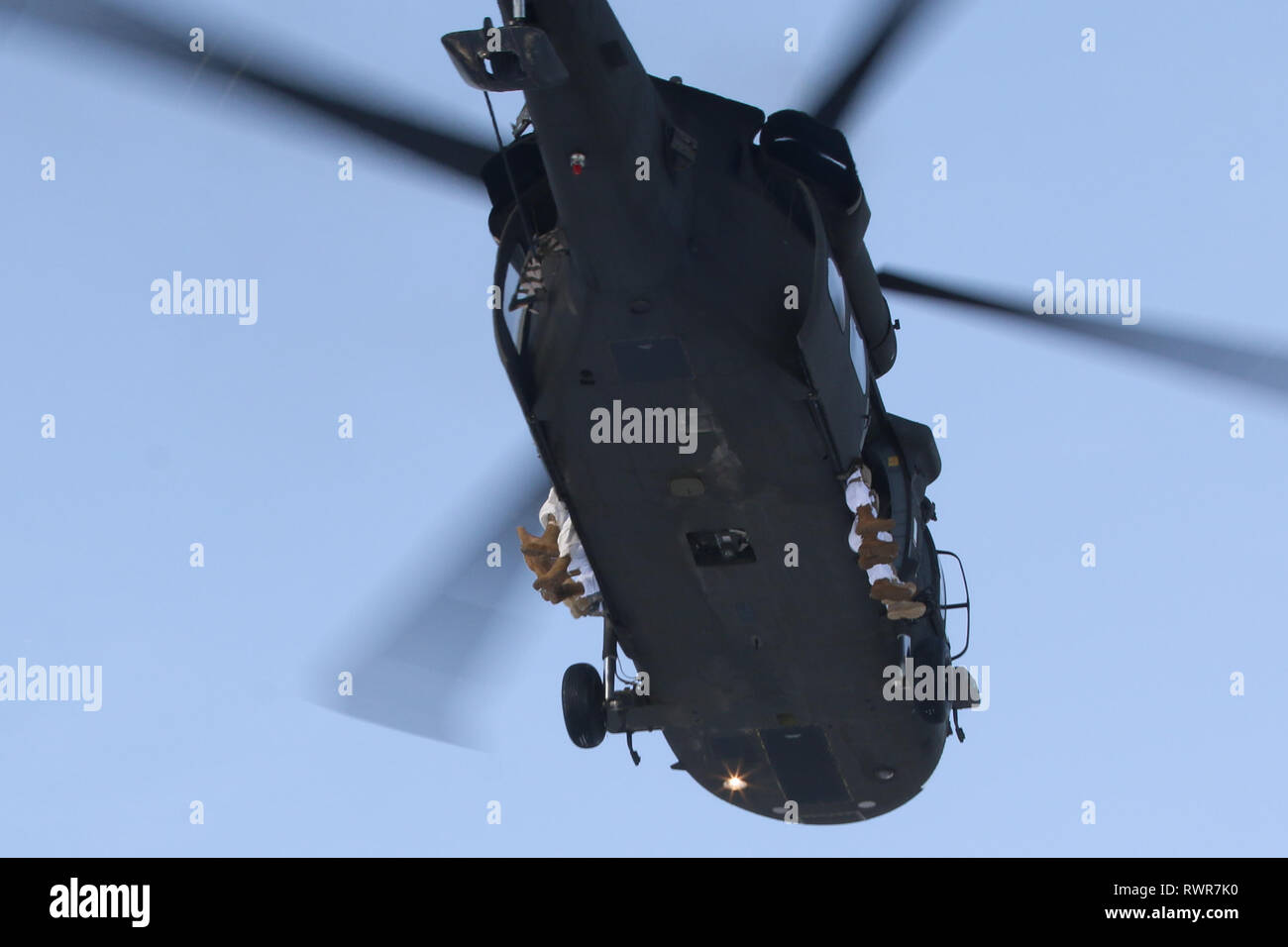 Paratroopers with 4th Infantry Brigade Combat Team (Airborne), 25th Infantry Division, U.S. Army Alaska, sit on the side of a UH-60 Blackhawk during airborne operations at Joint Base Elmendorf-Richardson, Alaska, March 6, 2019. Approximately 300 paratroopers took turns jumping onto Alaska’s snow covered drop zone from the helicopters. When jumping from a Blackhawk, paratroopers sit on the side of the helicopter with open doors.  (U.S. Army photo by Sgt. Alex Skripnichuk) Stock Photo