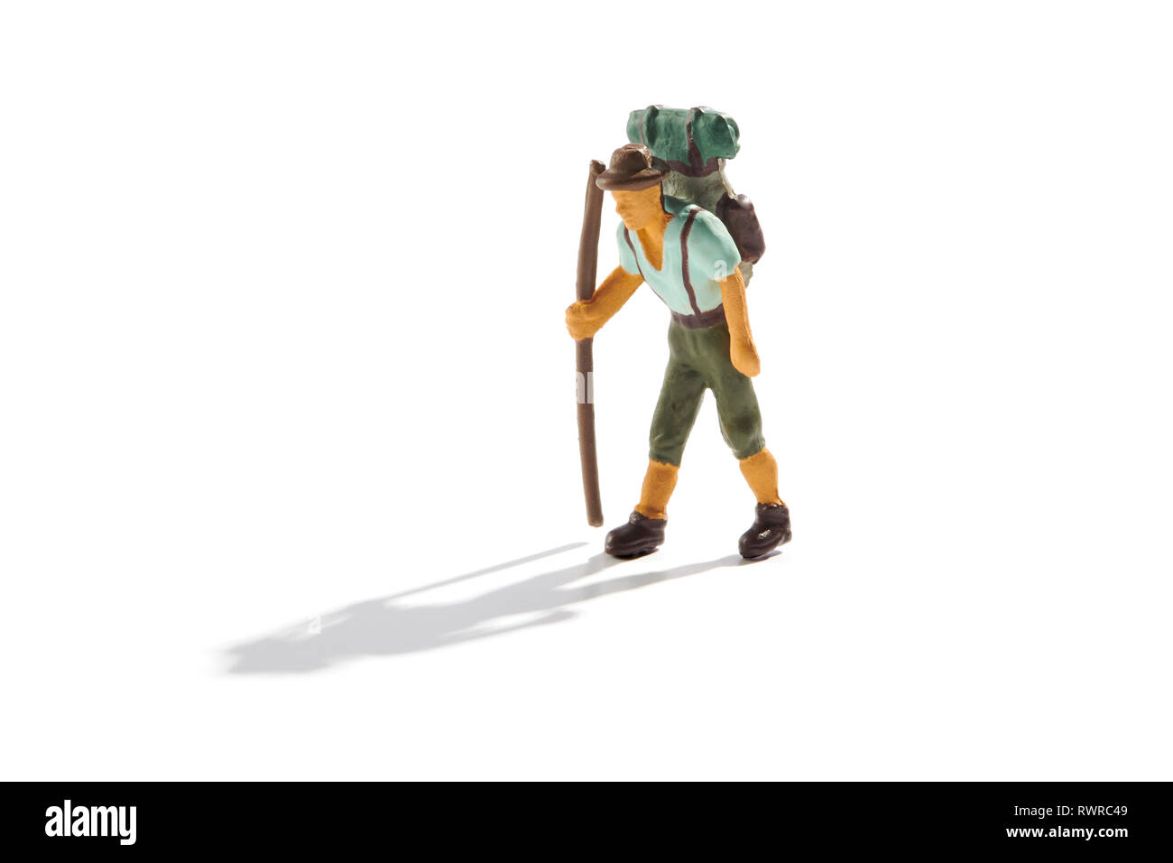 Miniature male backpacker with rucksack trekking on mountains with his hiking boots and stick isolated on white with shadow and copy space Stock Photo