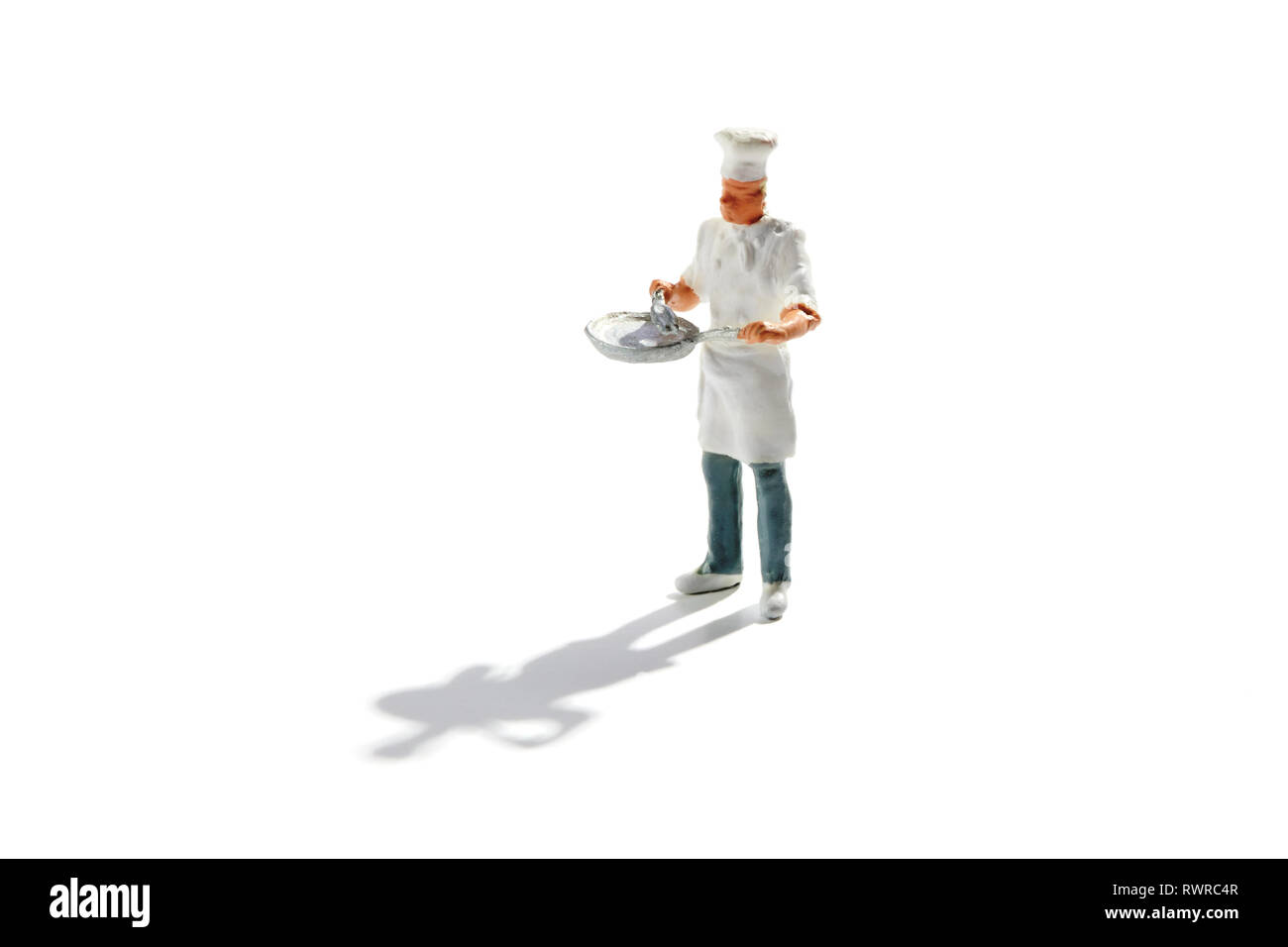 Miniature master chef in toque and apron with a pan in his hands isolated on white with copy space and shadow Stock Photo