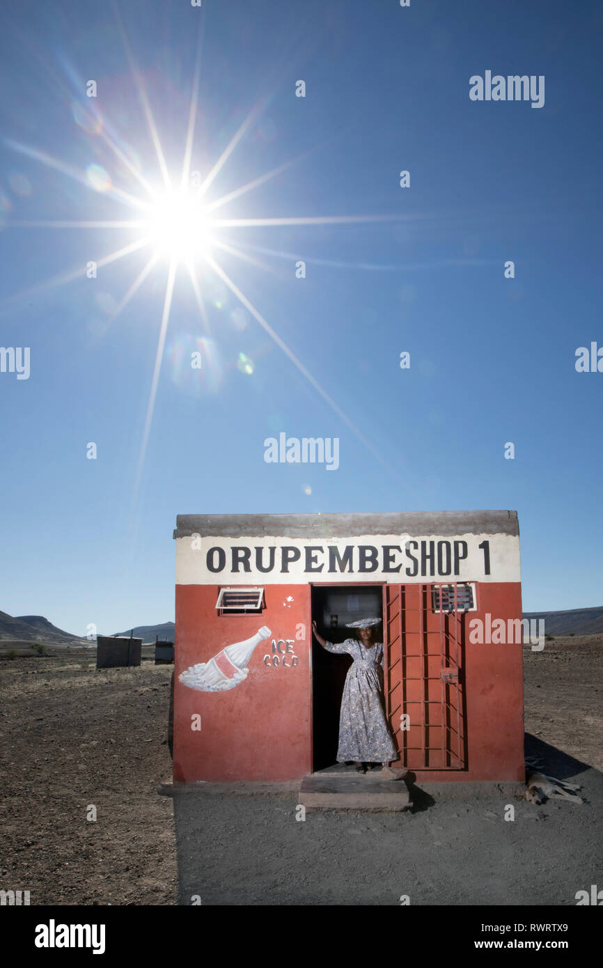 A Herero woman by a shop in the arid Kunene Region of northern Namibia. Stock Photo