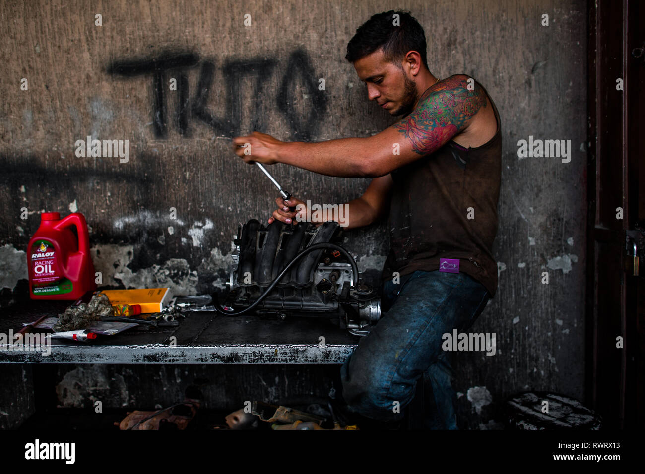A Colombian car mechanic works on an engine in a car repair shop in Barrio Triste, Medellín, Colombia. Stock Photo