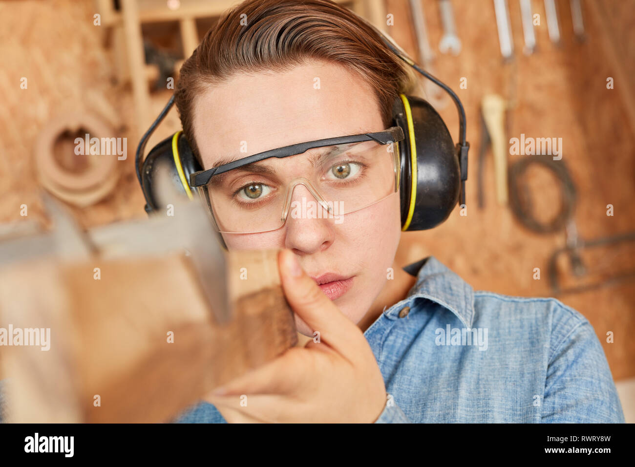 Woman as a carpenter apprentice while measuring wood board with caliper Stock Photo