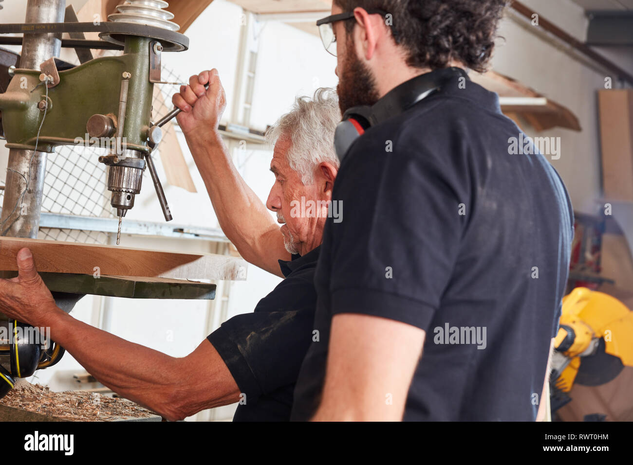 Apprentice observes senior carpenter while working with wood on drill Stock Photo