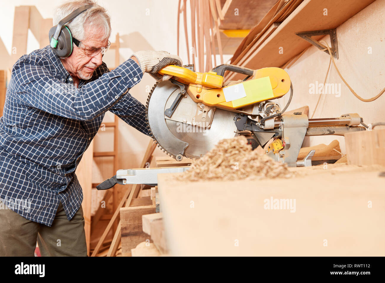 Old carpenter master at the woodworking at the chop saw in the