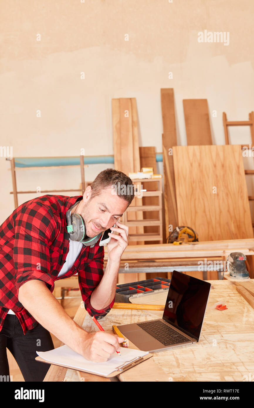Young man as a craftsman using mobile phone and laptop computer while scheduling Stock Photo
