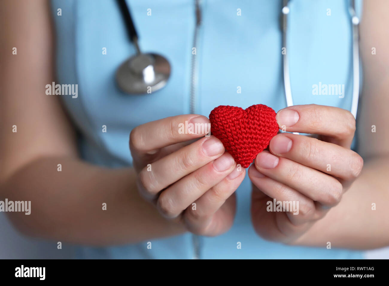 Cardiology and health care, woman doctor holding red knitted heart in hands. Concept of cardiologist, treatment of heart disease in the clinic Stock Photo