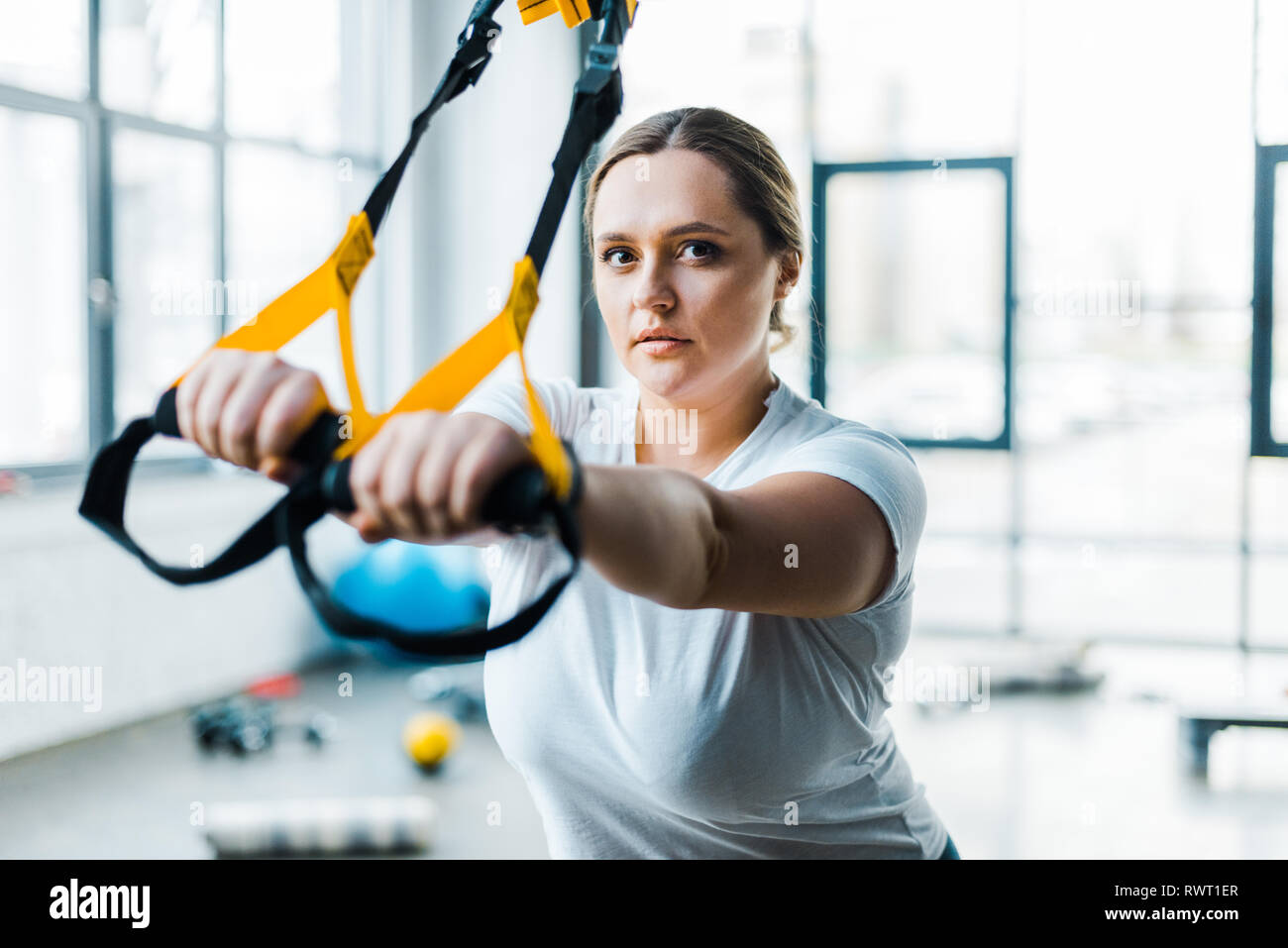 confident overweight woman training arms with suspension straps in gym