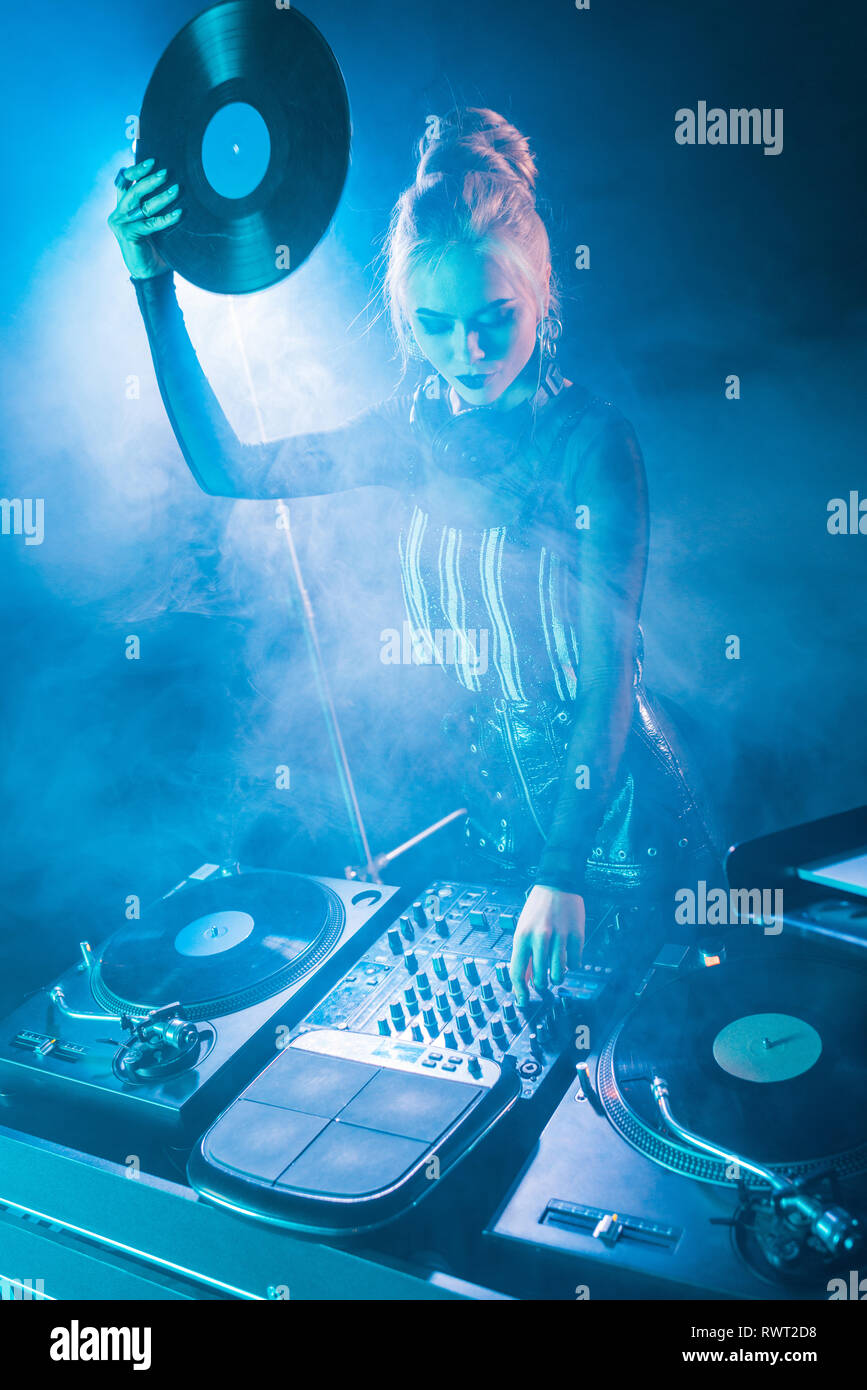 blonde dj girl looking at dj equipment and holding retro vinyl record