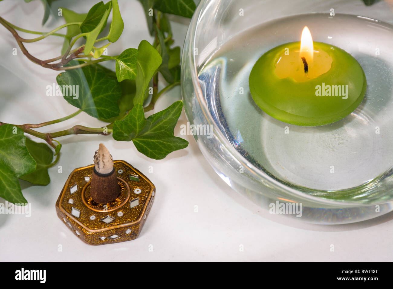 Lit candle with incense and some leaves, in a bathroom or a spa, with white background Stock