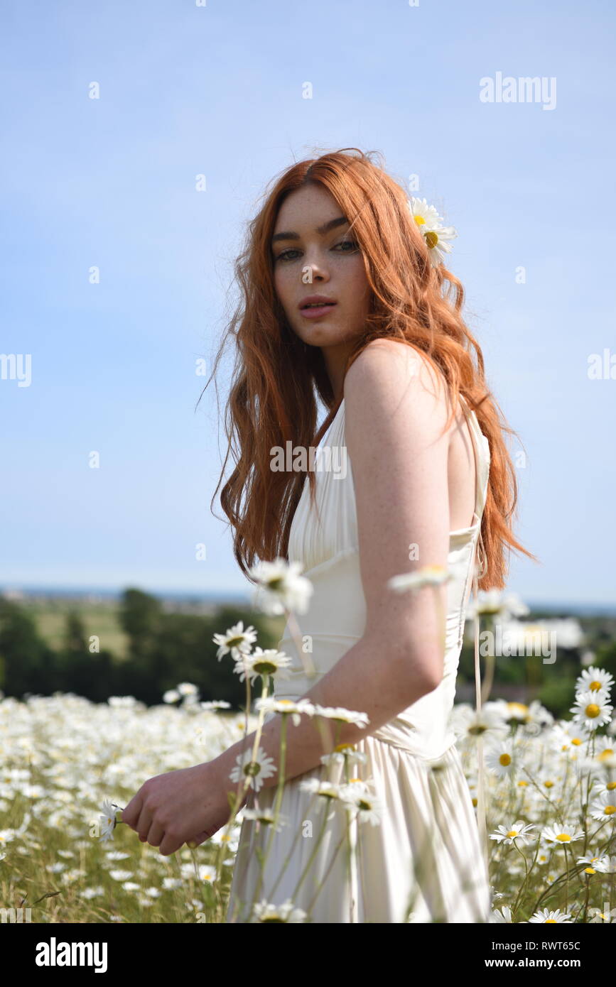 A beautiful red haired girl in a long white dress poses in the middle ...