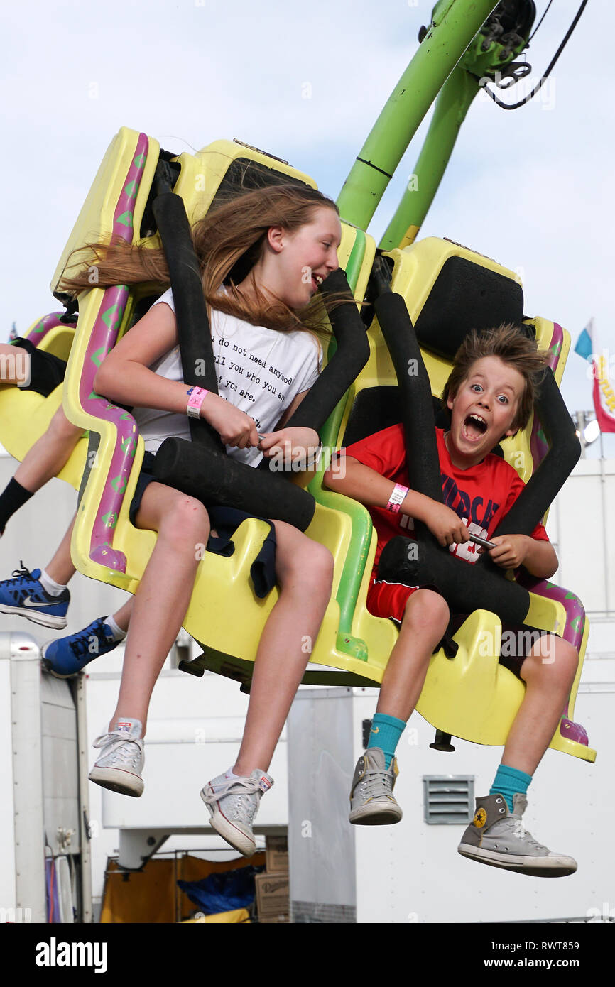 Two kids ride an Amusement park rides at a local fairgrounds. Stock Photo